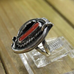 May include: A silver ring with a red coral stone set in a silver band. The ring is designed with a twisted rope pattern around the stone.