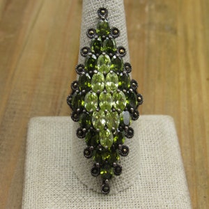 May include: A silver ring with a large green gemstone cluster in a teardrop shape. The ring is set with smaller green gemstones and black marcasite.