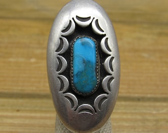 Pode incluir: Um anel de prata com uma pedra turquesa engastada em um design oval decorativo.