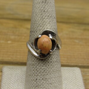 May include: A silver ring with a peach-colored stone set in a swirl design.