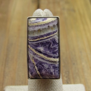 May include: A silver ring with a rectangular purple and white stone. The stone has a swirling pattern.