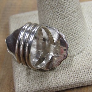 May include: Silver ring with a textured design. The ring is shown from the back, revealing the band and the open setting.
