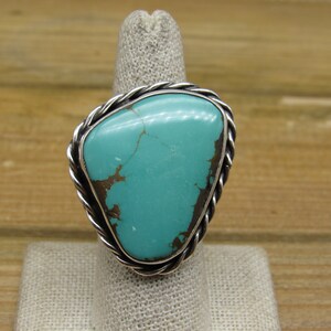 May include: A turquoise ring with a silver setting. The turquoise is a bright blue-green color and has a unique pattern of veins. The silver setting is a twisted rope design.