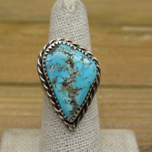 May include: A turquoise ring with a silver setting. The turquoise is a bright blue color with a lot of matrix. The setting is a twisted rope design.