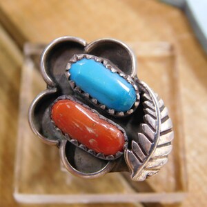 May include: A silver ring with a turquoise and coral stone design. The ring has a flower-shaped setting with a leaf detail.
