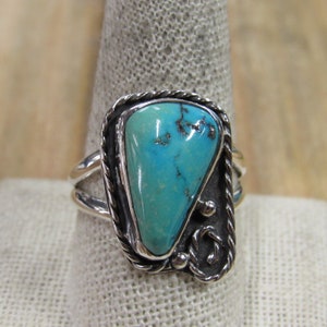 May include: Sterling silver ring featuring a vibrant turquoise stone. The turquoise is a bright blue-green color, set in a decorative silver frame with a twisted rope design and ornate accents. The ring has a split shank.