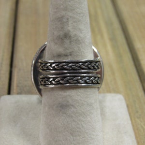May include: A silver ring with a braided band. The ring is on a white display stand.