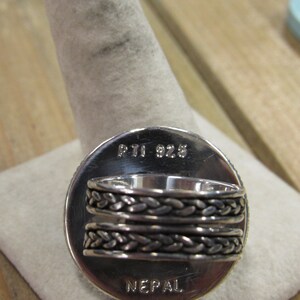 May include: Silver ring with a braided band and a round face that says "PTI 925 NEPAL" on the back.