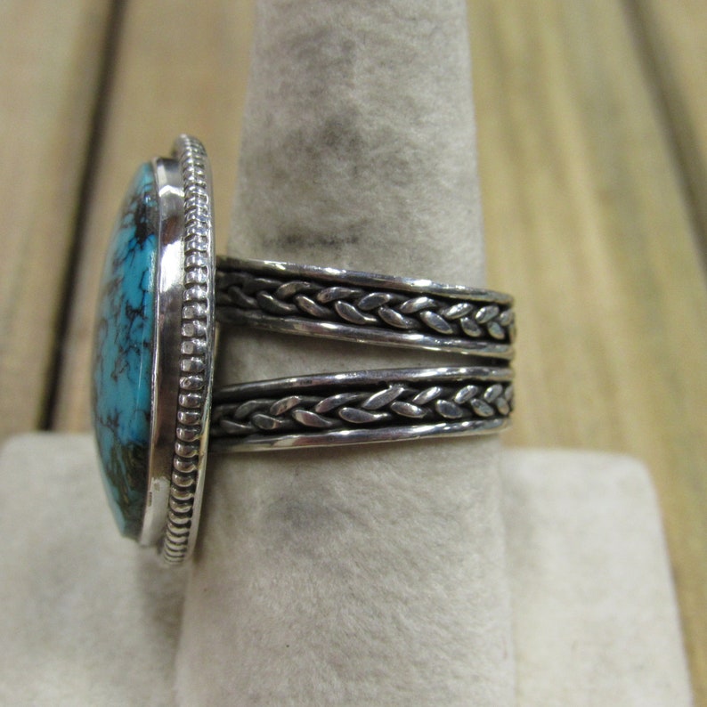 May include: A silver ring with a braided band and a large oval turquoise stone.