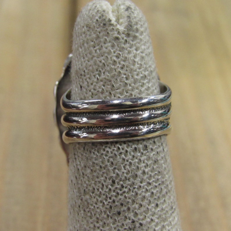 May include: Silver ring with three bands, each with a textured surface. The ring is on a fabric display stand.