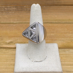 May include: A silver-toned ring with a geometric design. The ring features a triangular section with openwork and clear stones, and a smooth, white, rectangular stone. The ring is displayed on a white ring holder.