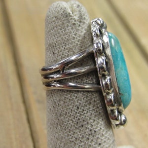 May include: A silver ring with a turquoise stone set in a silver bezel. The ring has a triple band design.