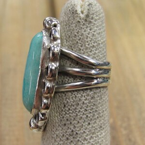 May include: A silver ring with a turquoise stone set in a decorative bezel. The band is made of three twisted wires.