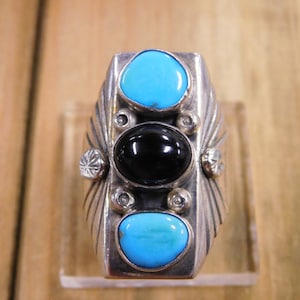 May include: A silver ring with three stones. The center stone is black, and the two stones on either side are turquoise.