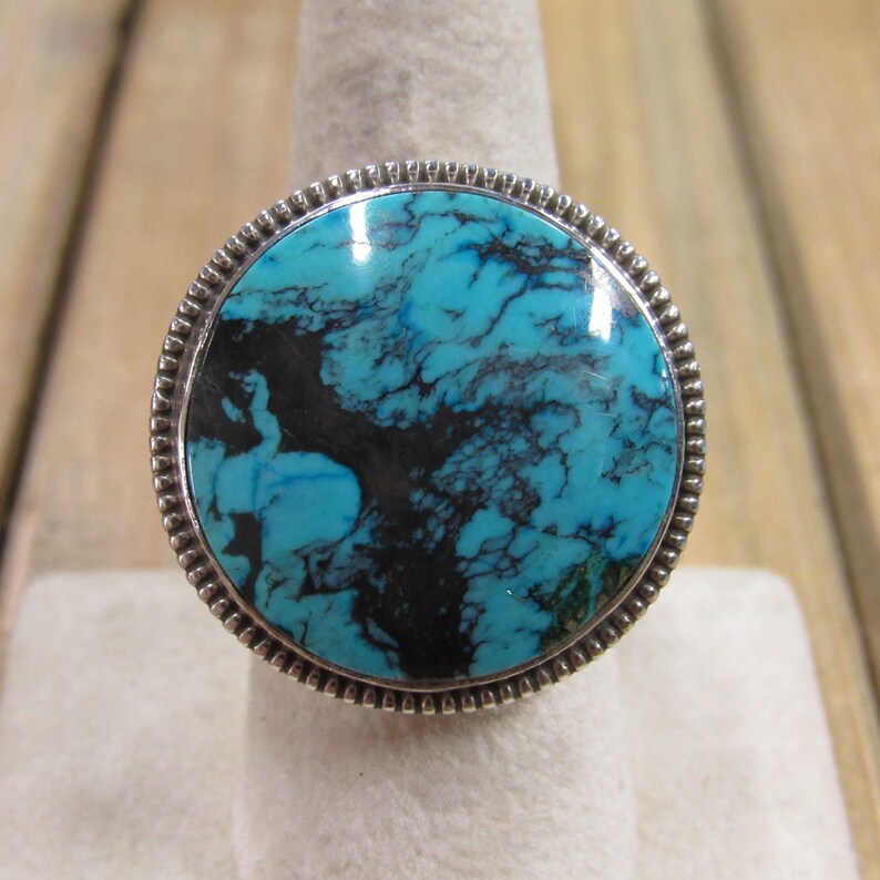 May include: A silver ring with a large turquoise stone set in a round bezel. The turquoise is a deep blue with black veins.