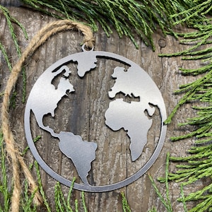 May include: A silver metal ornament shaped like the Earth. The ornament is hanging from a twine string and is on a wooden background.