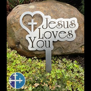 Puede incluir: Estaca de jard&iacute;n de metal con forma de coraz&oacute;n que contiene una cruz y las palabras "Jes&uacute;s te ama".