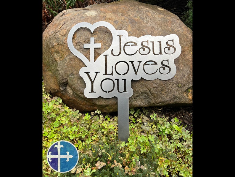 Puede incluir: Estaca de jard&iacute;n de metal con forma de coraz&oacute;n que contiene una cruz y las palabras "Jes&uacute;s te ama".