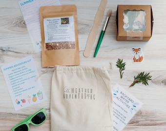 May include: A summer adventure kit with a white canvas bag, a brown paper bag with a pinecone bird feeder, a small brown box with a clear window, a green paintbrush, a wooden stick, a green leafy branch, a fox sticker, and a sheet of paper with the text "Backyard Water Activities".