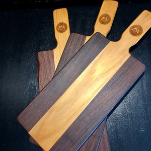 May include: Three wooden cutting boards with a light wood center and dark wood edges. Each board has a handle and the initials "AW" are engraved on the handle.