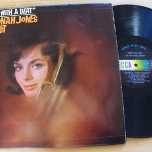 May include: A vintage vinyl record album cover featuring a woman holding a trumpet. The album is titled "Sweet With A Beat" by The Jonah Jones Quartet. The album cover is a warm orange color with a black and white photo of the woman.