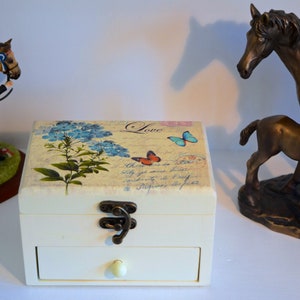 May include: A white wooden box with a drawer, decorated with a floral design and butterflies. The box has a brass latch and the word "Love" is printed on the top.