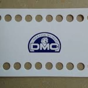 Puede incluir: Telar de punto de plástico blanco con 20 agujeros, con un logotipo DMC azul y blanco con el texto "Creative World DMC".