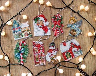 May include: Eight handmade Christmas ornaments featuring a variety of winter themes, including a snowman, a house, a candy cane, and Santa Claus. The ornaments are white with red, green, and blue accents.