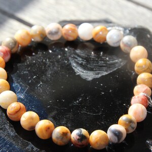 Peut inclure: Un bracelet composé de perles d'agate brunes, blanches et orange avec un charme argenté.