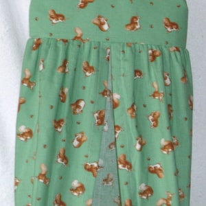 May include: A green fabric diaper stacker with a repeating pattern of brown and white squirrels. The stacker is hanging from a metal hanger and has a split front for easy access to diapers. The fabric is a light green color.