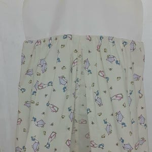 May include: A white fabric hanging organizer with a white hanger. The fabric has a pattern of pink and blue ducks with yellow flowers on a cream background.