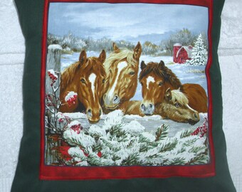 May include: Four brown horses with white markings on their faces are looking over a wooden fence. The horses are in a snowy winter scene with a red barn in the background. The horses are surrounded by evergreen trees with snow on the branches.
