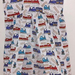 May include: White fabric garment bag with a repeating pattern of red and blue trains, train tracks, and clouds. The bag is hanging from a metal hanger. The overall theme is transportation.