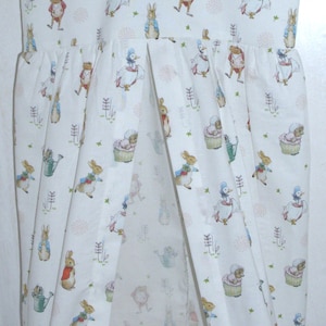 May include: A white fabric hanging organizer with a Peter Rabbit print. The organizer has a hanger at the top and multiple pockets for storage.