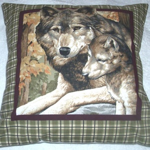 May include: Square decorative pillow featuring a detailed image of two wolves in a forest setting. The central image is framed with a burgundy border and set against a green and black plaid pattern. The wolves are depicted in shades of brown and gray.