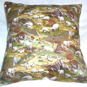 May include: A square throw pillow with a green, brown, and white patterned fabric featuring a flock of sheep in a field. The pillow is made of a soft, comfortable material and is perfect for adding a touch of rustic charm to any room.