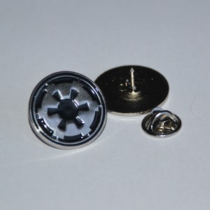 Può includere: Uno spillo d'argento con un simbolo imperiale nero e bianco di Star Wars. Lo spillo ha un retro in argento e una chiusura di sicurezza.