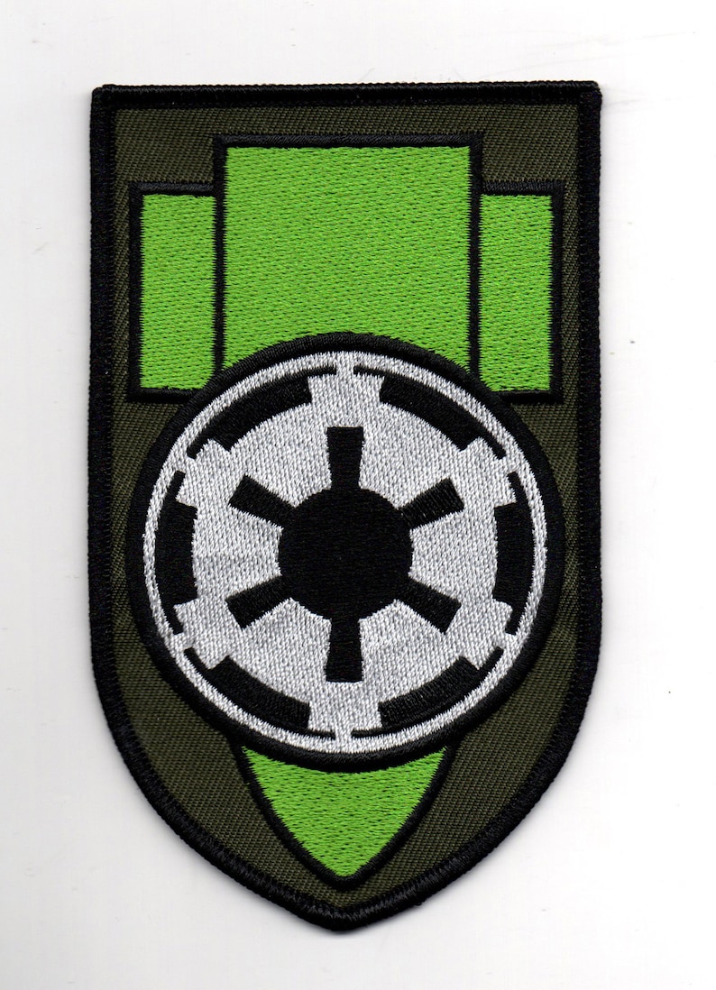 Puede incluir: Un parche bordado verde y negro con un s&iacute;mbolo imperial blanco y negro de Star Wars. El parche tiene forma de escudo con una punta verde en la parte inferior.