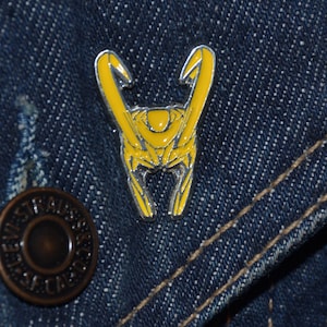 May include: A yellow metal pin featuring a design of Loki's horns from the Marvel Cinematic Universe.