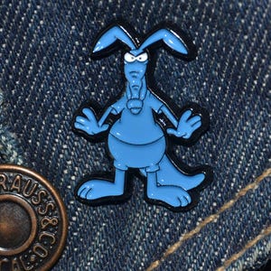 May include: Blue enamel pin featuring a cartoon aardvark with an angry expression. The aardvark is wearing a blue shirt and has black outlines.