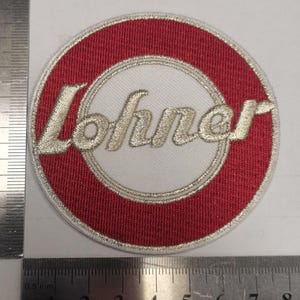 Puede incluir: Parche bordado circular con un anillo exterior rojo y un centro blanco. La palabra "Lohner" está bordada en cursiva en el centro del parche. El parche tiene aproximadamente 7,6 cm de diámetro.