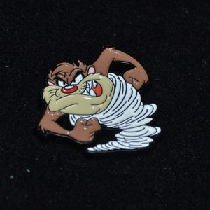 Puede incluir: Un personaje de dibujos animados marrón y blanco, Taz el Demonio de Tasmania, está representado en un tornado giratorio. El personaje tiene una expresión amenazante con dientes afilados y una boca abierta de par en par.