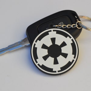 Può includere: Una chiave per auto nera con una chiave argentata e un portachiavi nero e bianco con il simbolo imperiale di Star Wars.