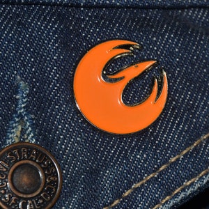 Op de afbeelding: Oranje en zilveren Rebel Alliance-symboolspeld op een blauw denim jack.
