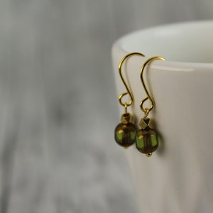 Könnte beinhalten: Ein Paar goldene Ohrhänger mit grünen Glasperlen. Die Perlen haben eine schimmernde, irisierende Oberfläche.