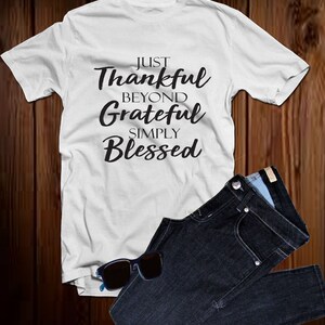 以下が含まれることがあります： 黒い文字で「Just Thankful Beyond Grateful Simply Blessed」とプリントされた白いTシャツです。
