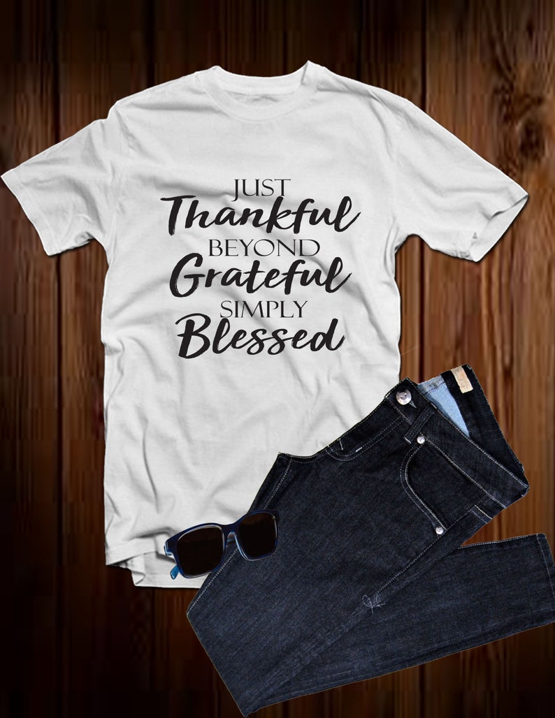 以下が含まれることがあります： 黒い文字で「Just Thankful Beyond Grateful Simply Blessed」とプリントされた白いTシャツです。