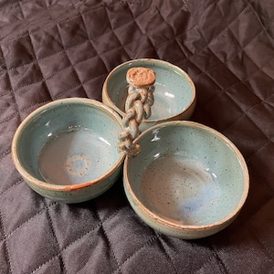 May include: A three-section ceramic serving dish with a braided handle. The dish is light blue with a speckled glaze and a white interior.