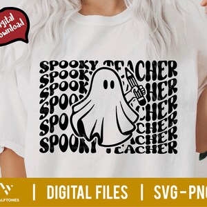 May include: A white t-shirt with a black and white graphic design of a ghost holding a pencil. The text "Spooky Teacher" is repeated in a wavy font around the ghost.