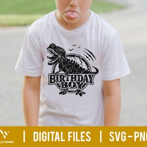 May include: A white t-shirt with a black graphic of a dinosaur with the text "Birthday Boy" in a circle.